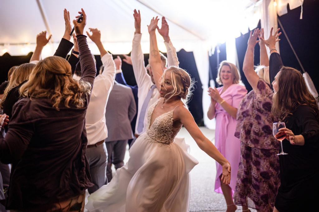 A bride and wedding guests dance under a tent.