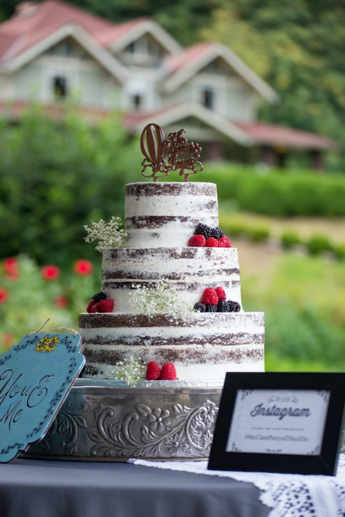 A wedding cake decorated with fresh fruit in front of an old house