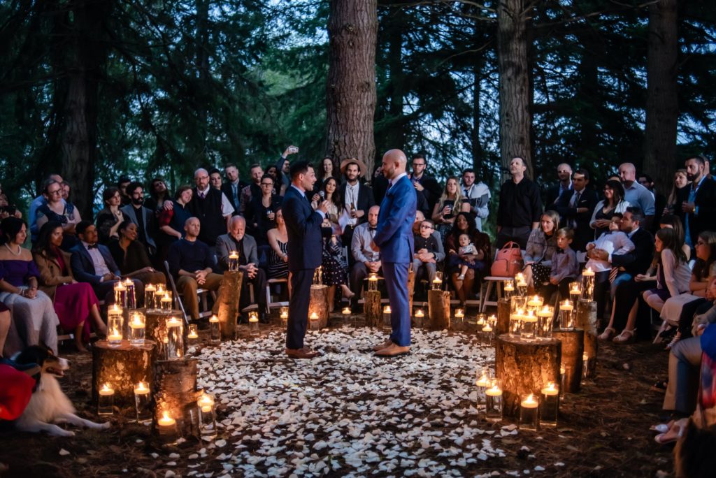 A groom reads his vows at a twilight ceremony surrounded by candles and rose petals